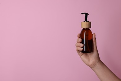 Woman holding bottle of cosmetic product on pink background, closeup. Space for text