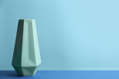 Stylish green ceramic vase on table against light blue background, space for text