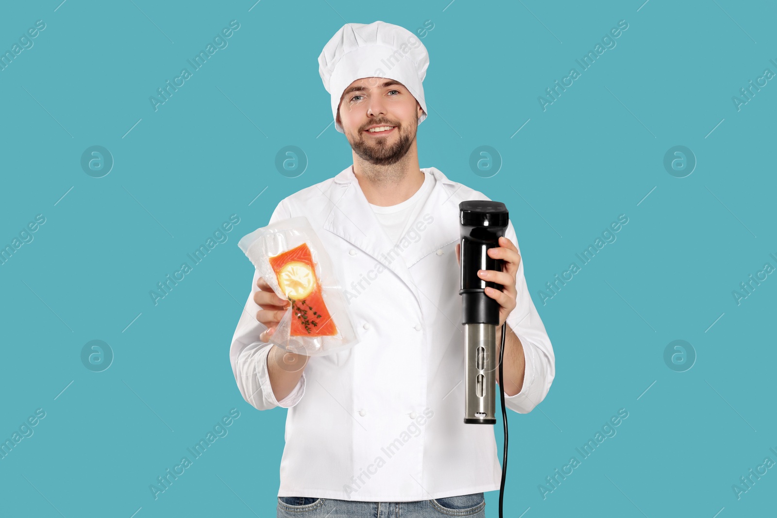 Photo of Smiling chef holding sous vide cooker and salmon in vacuum pack on light blue background