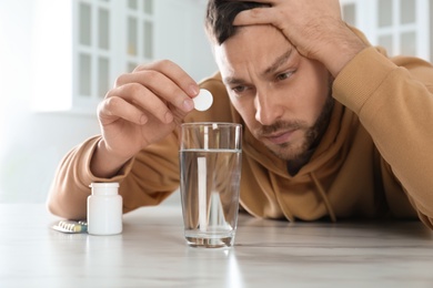 Man taking medicine for hangover at table in kitchen