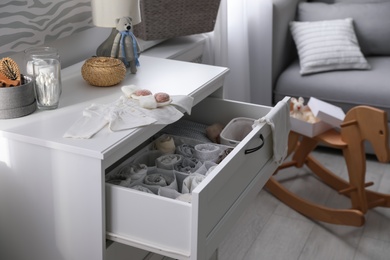 Modern open chest of drawers with baby clothes and accessories in room