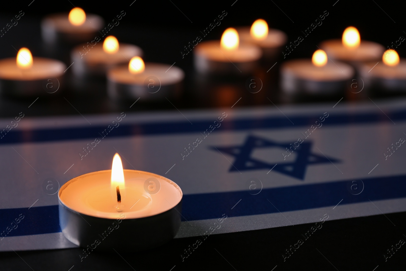 Photo of Burning candle and flag of Israel on black table. Holocaust memory day