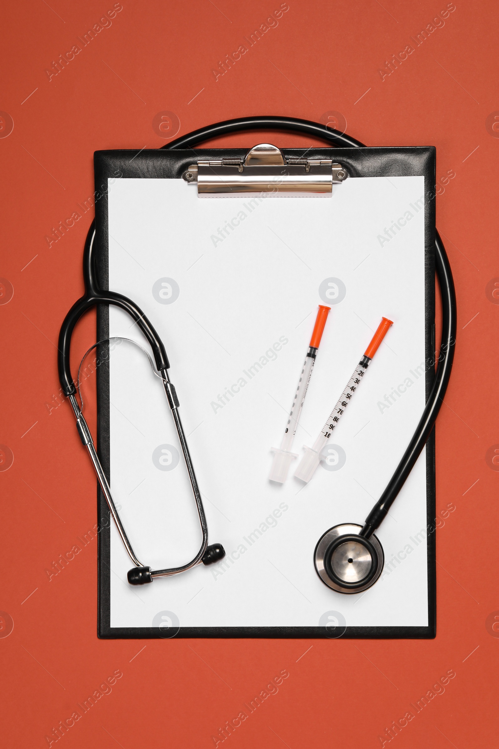 Photo of Stethoscope, syringes and clipboard on crimson background, top view. Medical tool