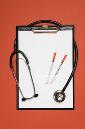 Stethoscope, syringes and clipboard on crimson background, top view. Medical tool