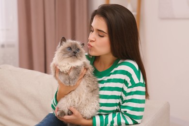 Woman kissing her cute cat on comfortable sofa at home