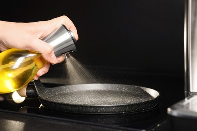 Woman spraying cooking oil onto frying pan on stove, closeup