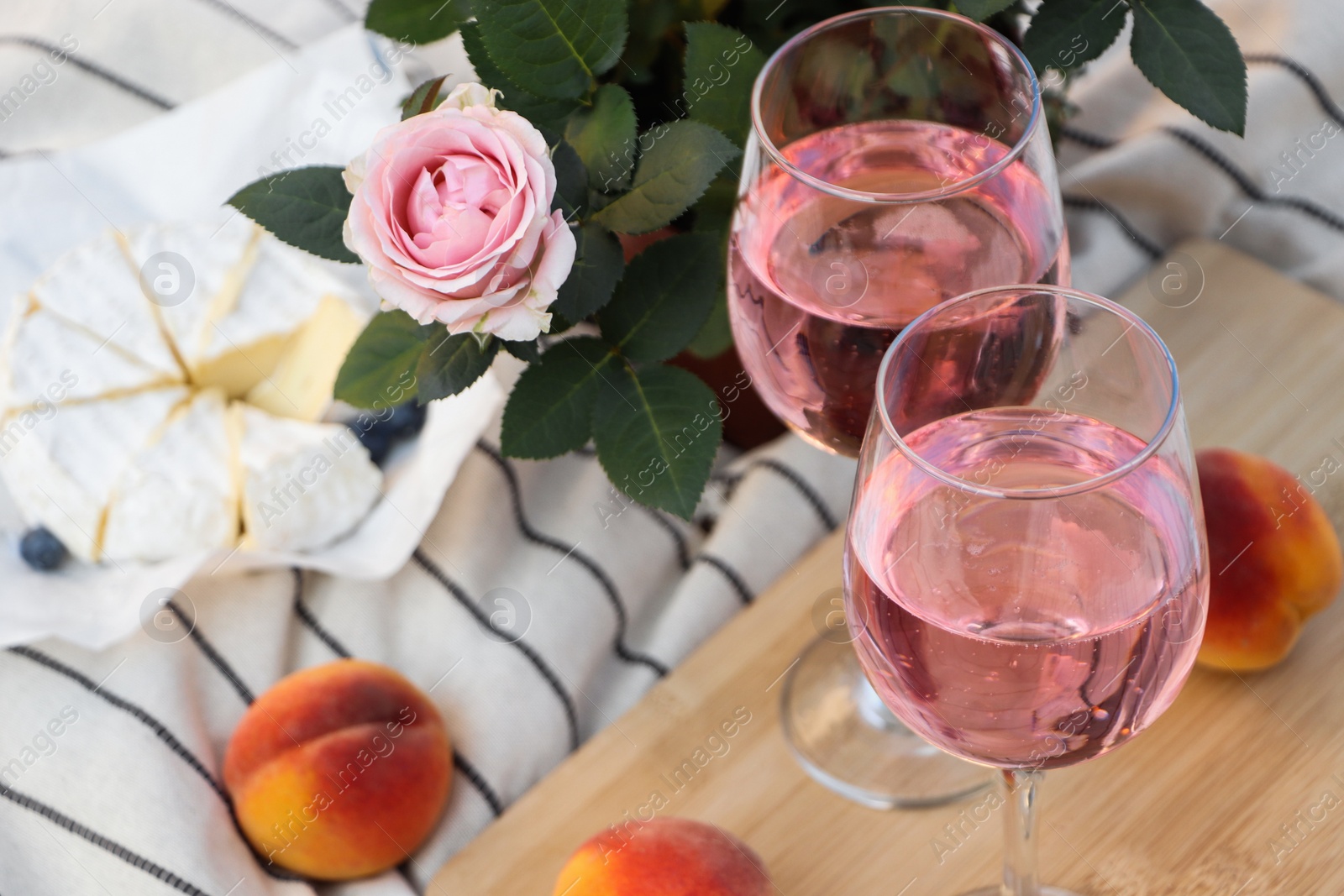 Photo of Glasses of delicious rose wine, flower and food on white picnic blanket