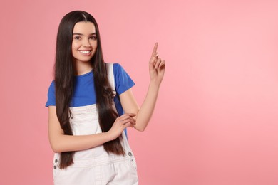 Teenage girl pointing at something on pink background. Space for text