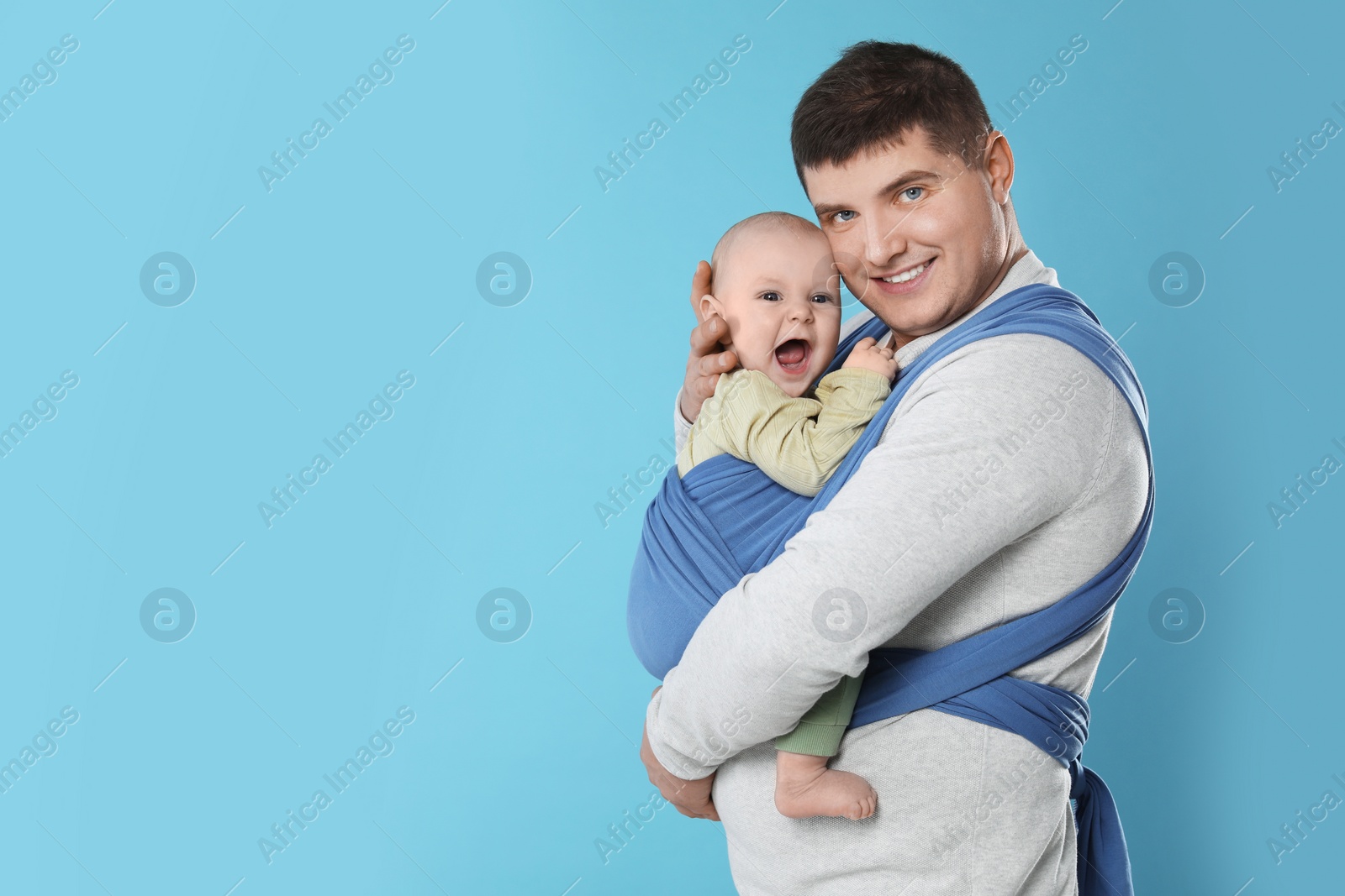 Photo of Father holding his child in sling (baby carrier) on light blue background. Space for text