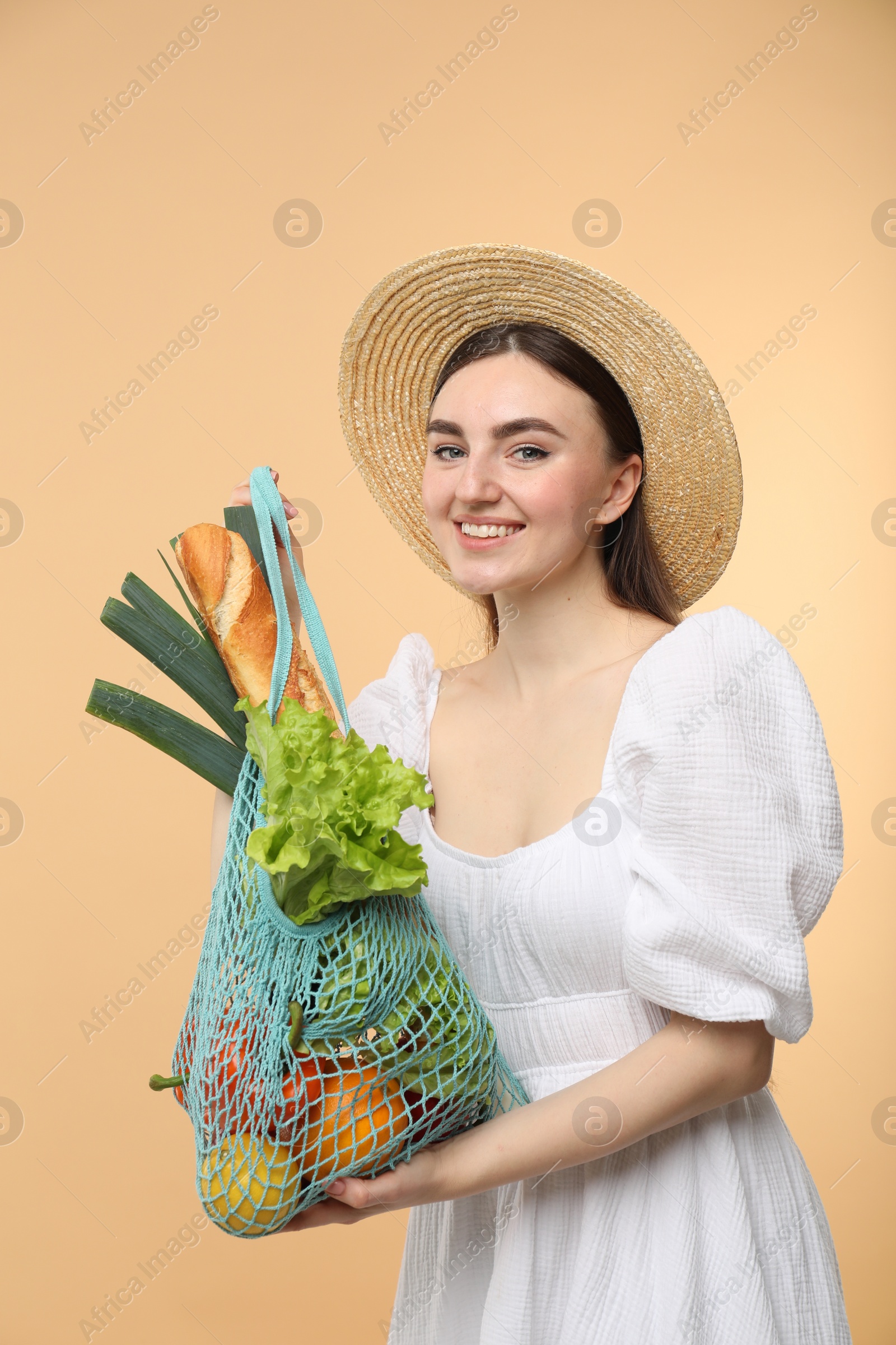 Photo of Woman with string bag of fresh vegetables and baguette on beige background