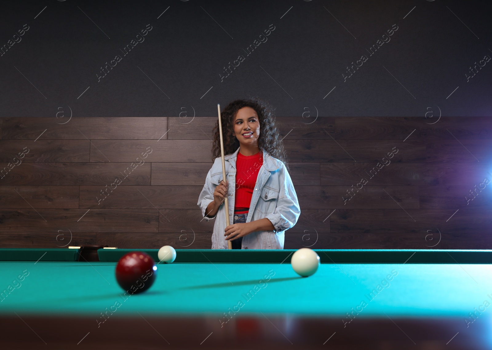 Photo of Young African-American woman with cue near billiard table indoors