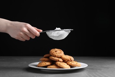 Woman with sieve sprinkling powdered sugar onto cookies at grey textured table, closeup