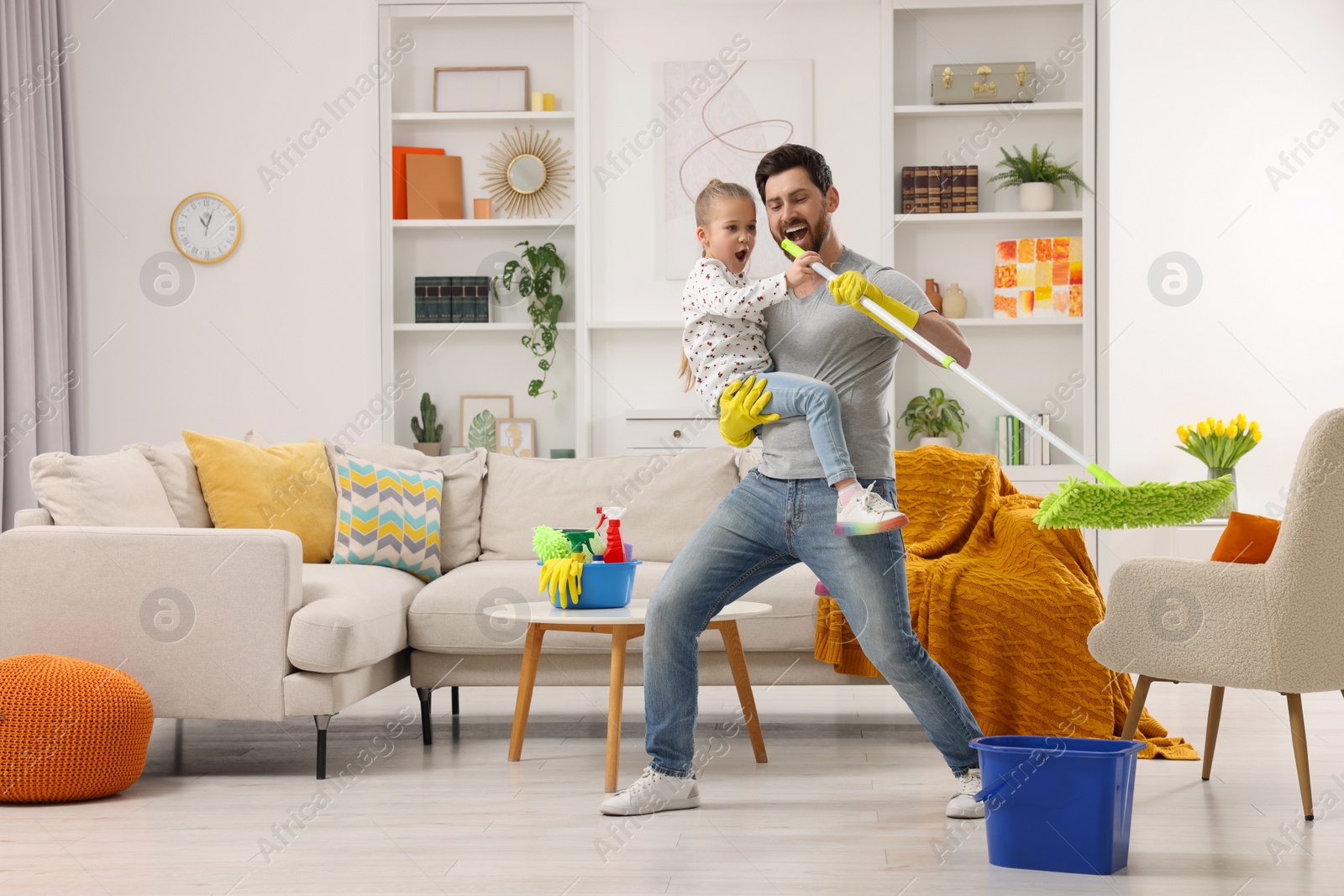 Photo of Spring cleaning. Father and daughter singing while tidying up together at home