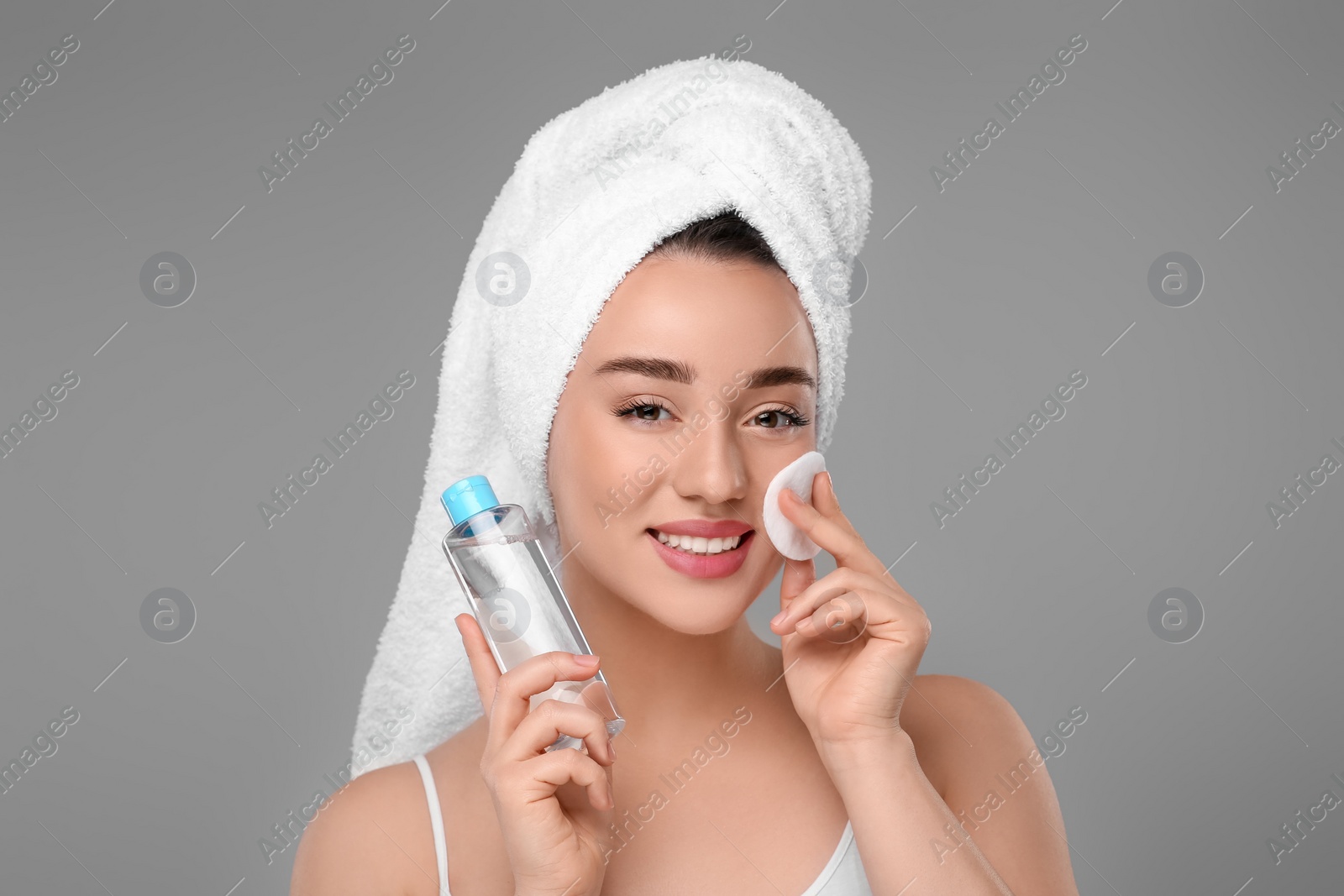 Photo of Beautiful woman in terry towel removing makeup with cotton pad on gray background