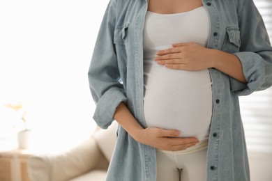 Photo of Pregnant woman touching her belly indoors, closeup