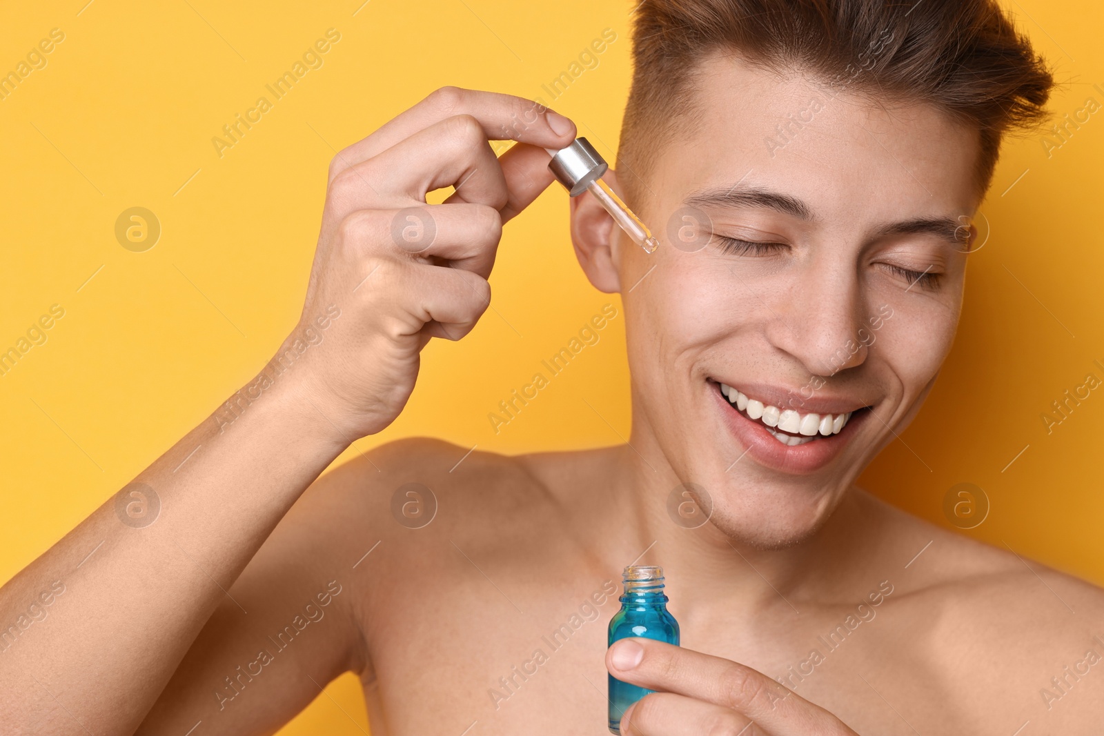 Photo of Handsome man applying serum onto his face on orange background