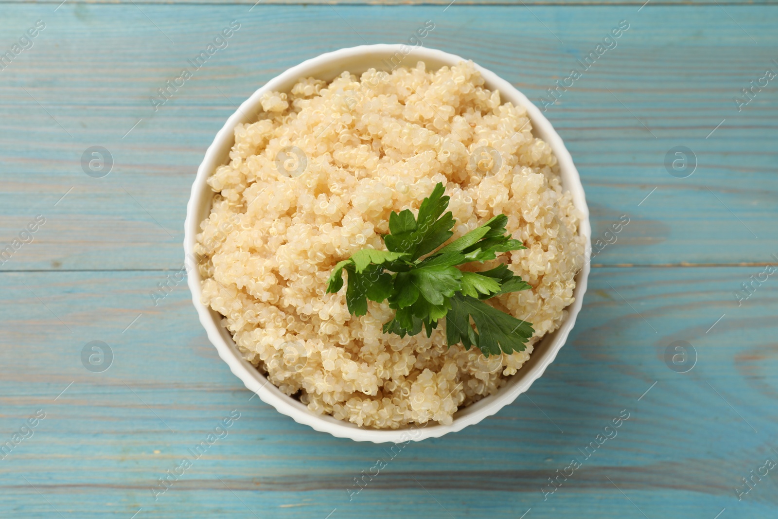 Photo of Tasty quinoa porridge with parsley in bowl on light blue wooden table, top view