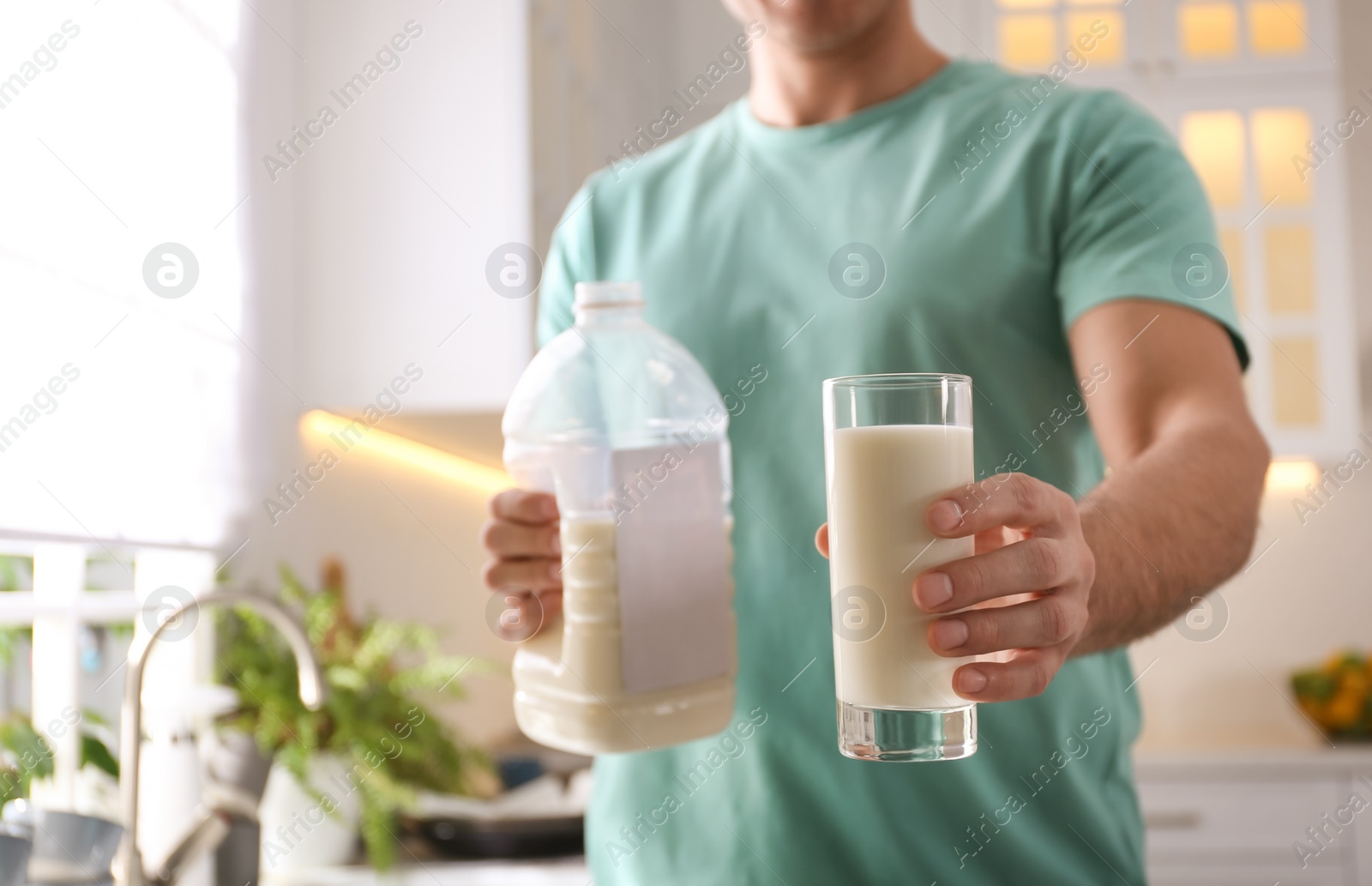 Photo of Man with gallon bottle of milk and glass in kitchen, closeup