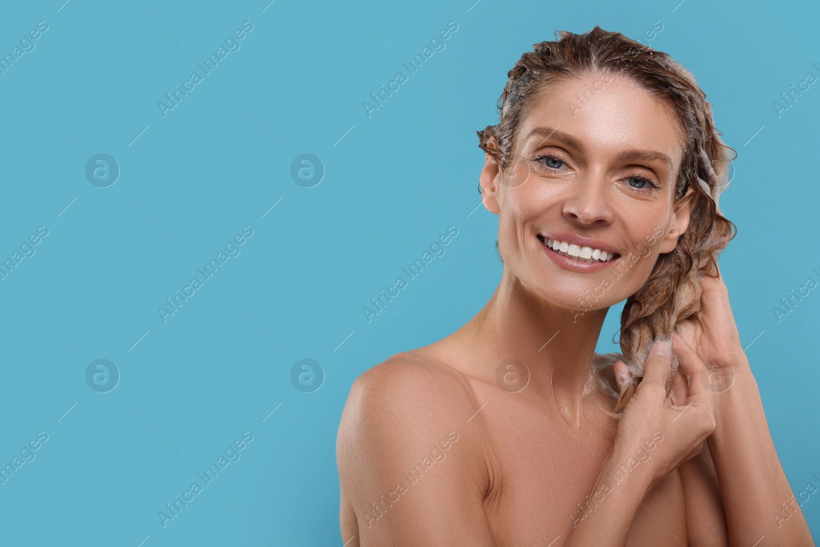 Photo of Portrait of beautiful happy woman washing hair on light blue background. Space for text