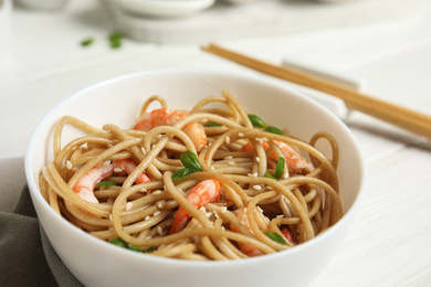 Photo of Tasty buckwheat noodles with shrimps in bowl on white wooden table, closeup