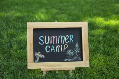 Photo of Blackboard with text SUMMER CAMP and drawings on green grass