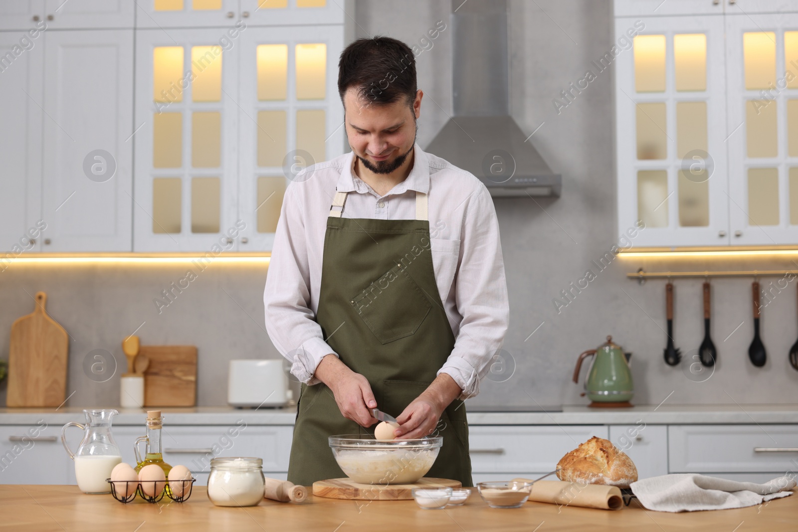 Photo of Making bread. Man putting raw egg into dough at wooden table in kitchen