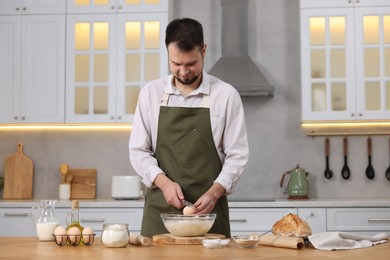 Making bread. Man putting raw egg into dough at wooden table in kitchen