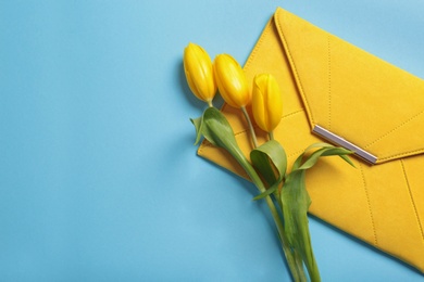 Photo of Flat lay composition with stylish woman's clutch and spring flowers on color background, space for text