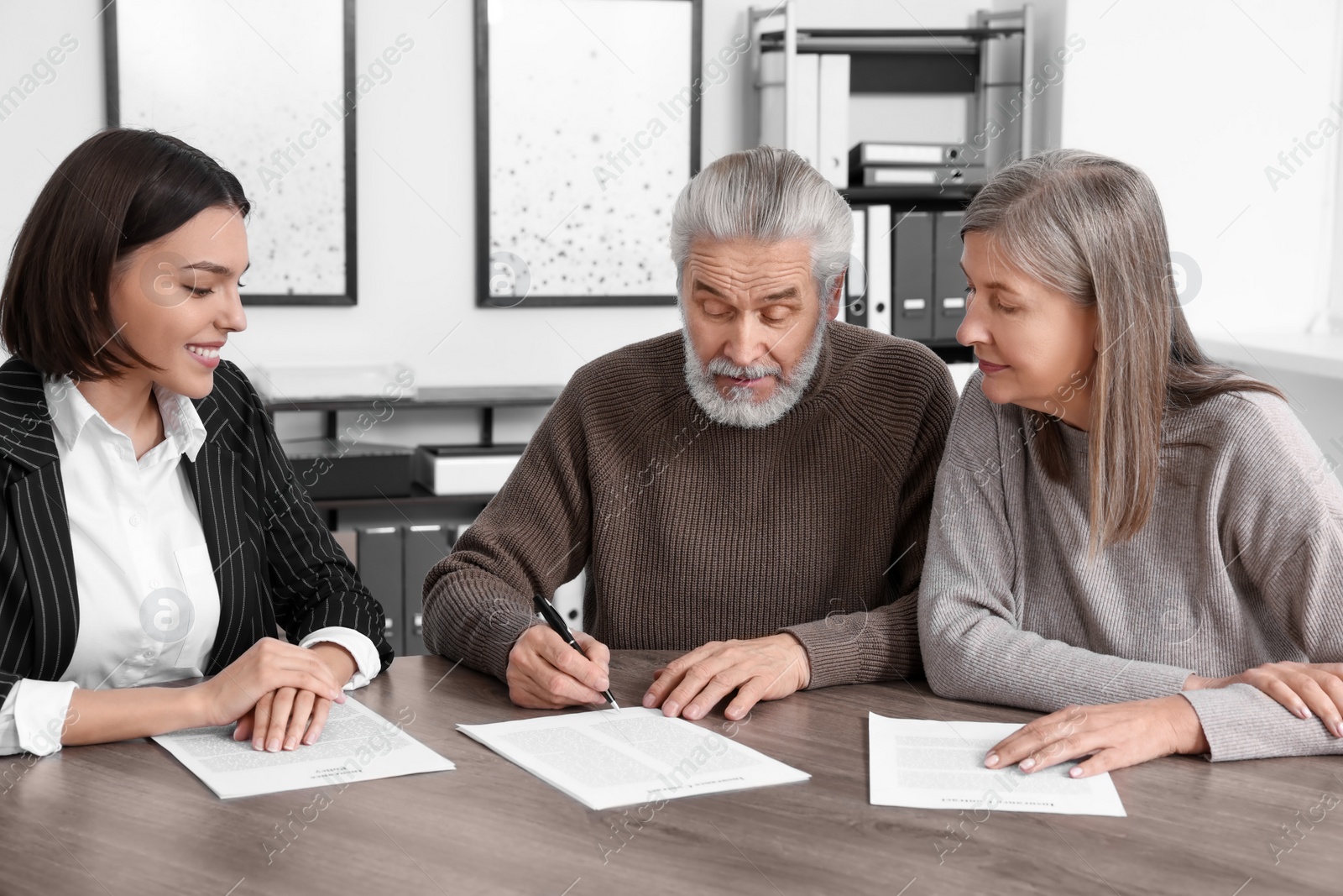 Photo of Elderly couple consulting insurance agent about pension plan at wooden table indoors