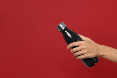 Woman holding modern dark  thermos on red background, closeup. Space for text