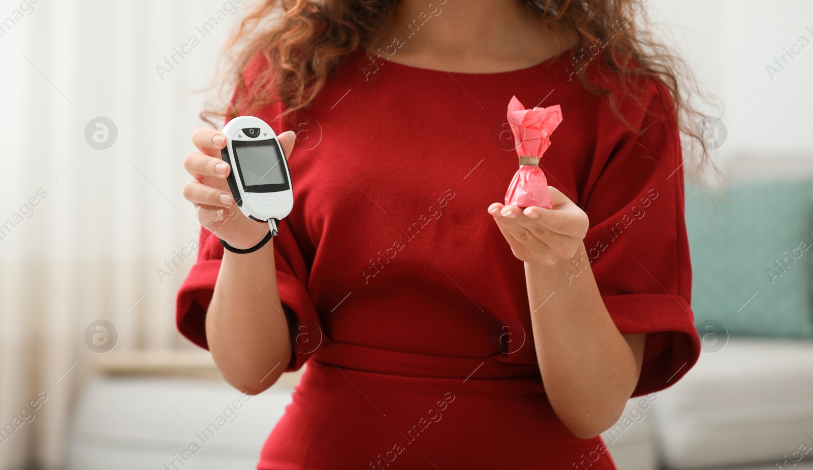 Photo of Young African-American woman holding digital glucometer and candy at home, closeup. Diabetes diet