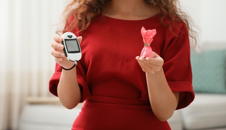 Young African-American woman holding digital glucometer and candy at home, closeup. Diabetes diet