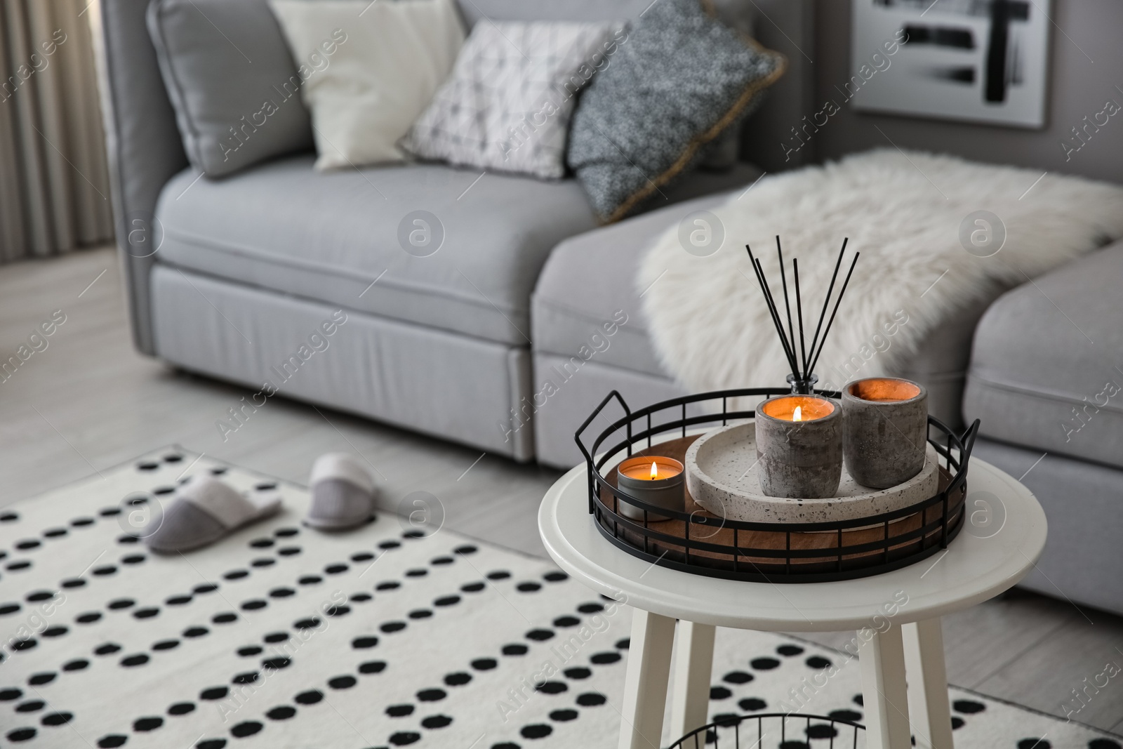 Photo of Candles and aroma reed diffuser on white table near grey sofa, space for text