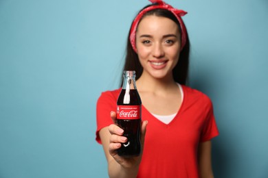 MYKOLAIV, UKRAINE - JANUARY 27, 2021: Young woman holding bottle of Coca-Cola against light blue background, focus on hand
