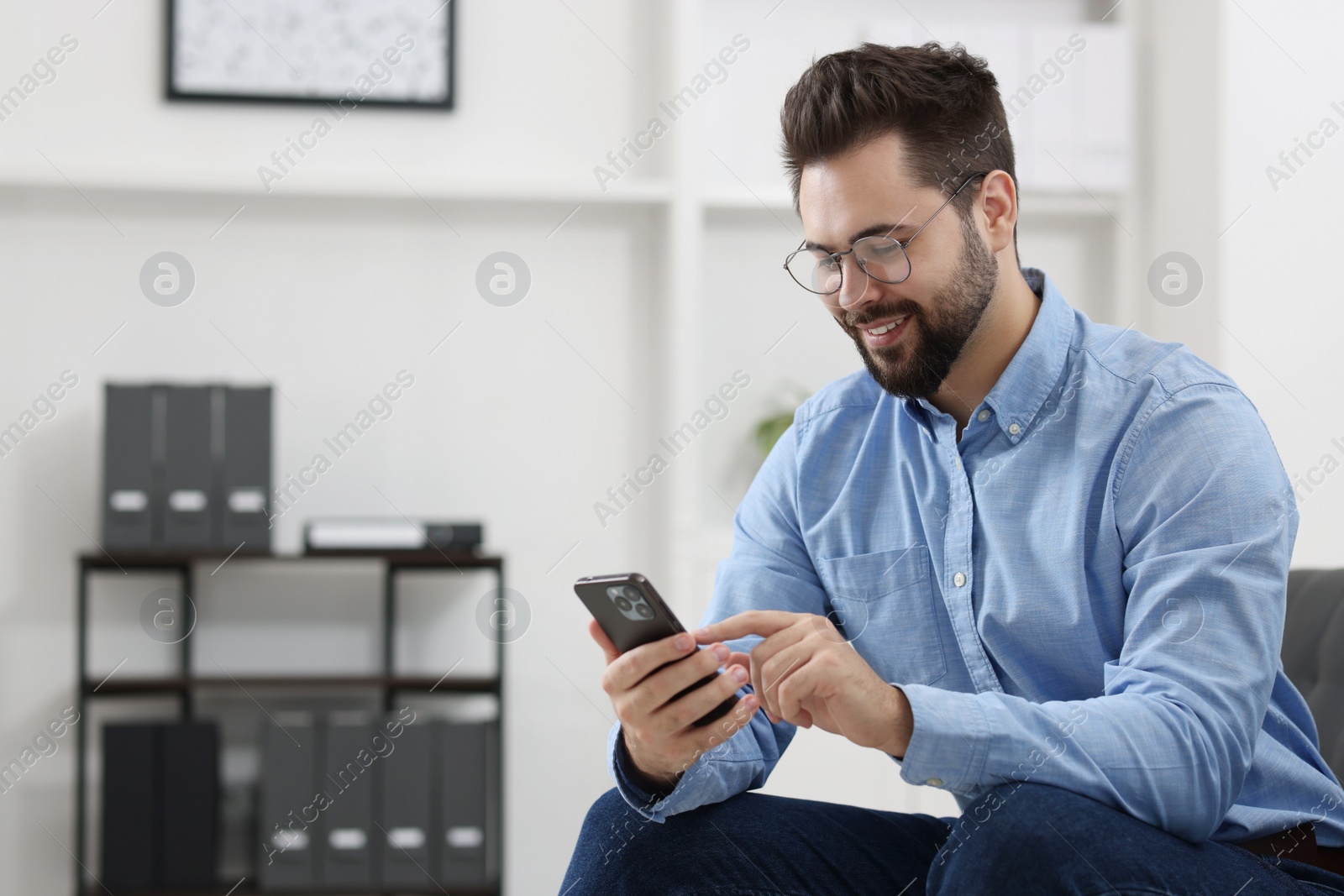 Photo of Handsome young man using smartphone in office, space for text