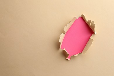 Photo of Hole in light beige paper on pink background, space for text