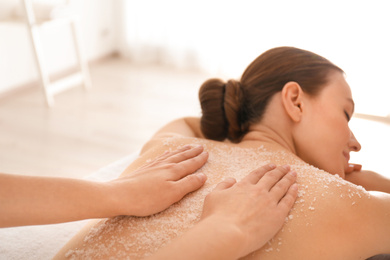 Young woman having body scrubbing procedure with sea salt in spa salon