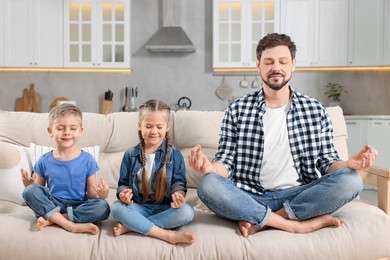Photo of Father with children meditating together on sofa at home. Harmony and zen