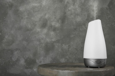 Photo of Modern essential oil diffuser on wooden table against grey background. Space for text