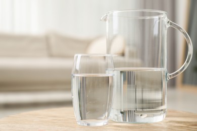 Photo of Jug and glass with clear water on wooden table indoors, closeup. Space for text
