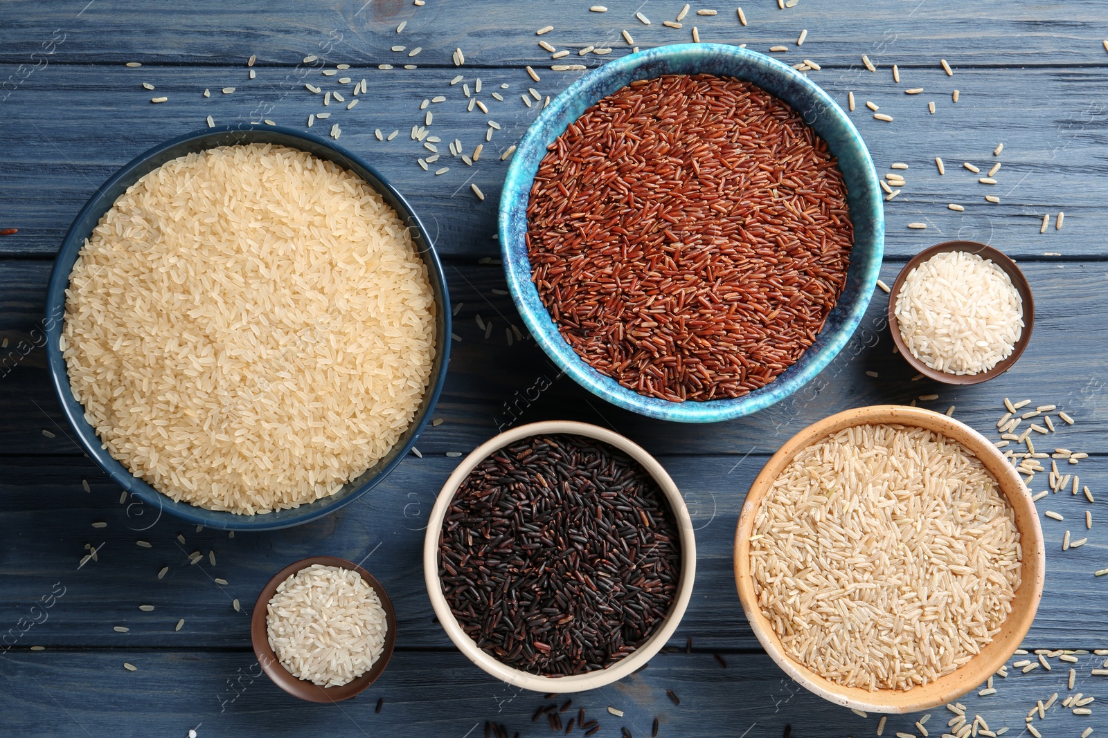 Photo of Flat lay composition with brown and other types of rice in bowls on color wooden background