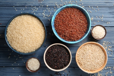 Photo of Flat lay composition with brown and other types of rice in bowls on color wooden background