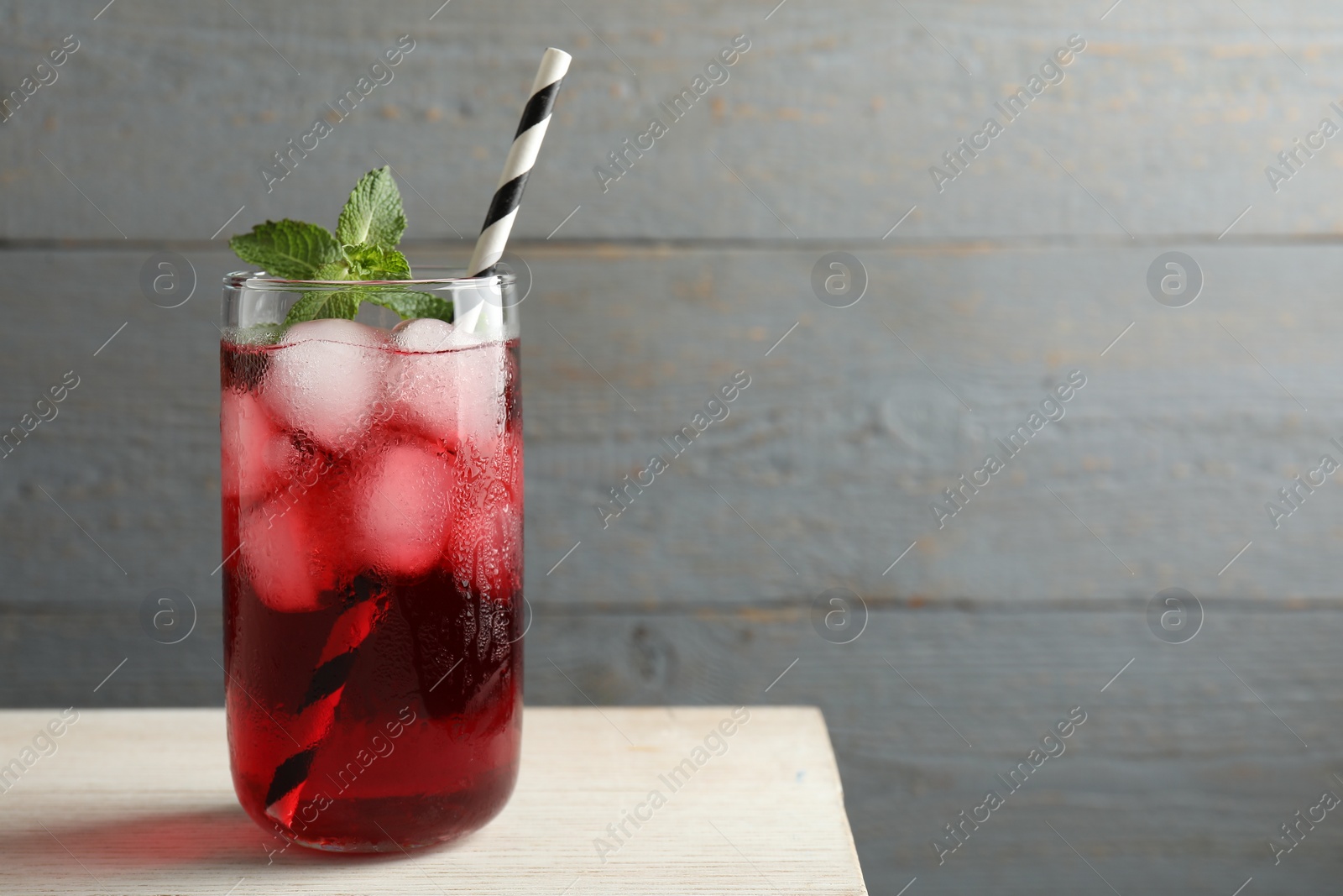 Photo of Glass of delicious iced hibiscus tea with mint and straw on wooden table, space for text