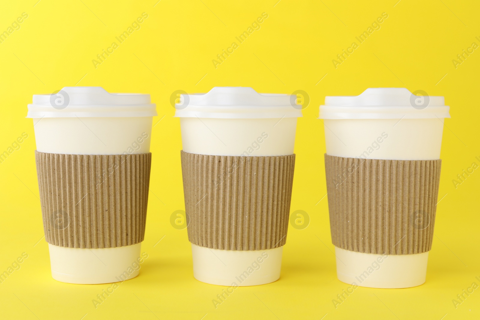 Photo of Paper cups with white lids on yellow background. Coffee to go