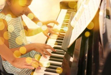 Image of Christmas and New Year music. Woman with little girl to play piano indoors. Bokeh effect