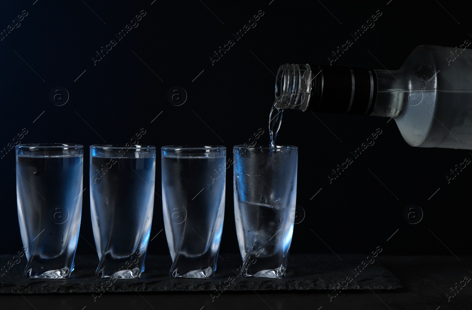 Photo of Pouring vodka from bottle in glass on black table