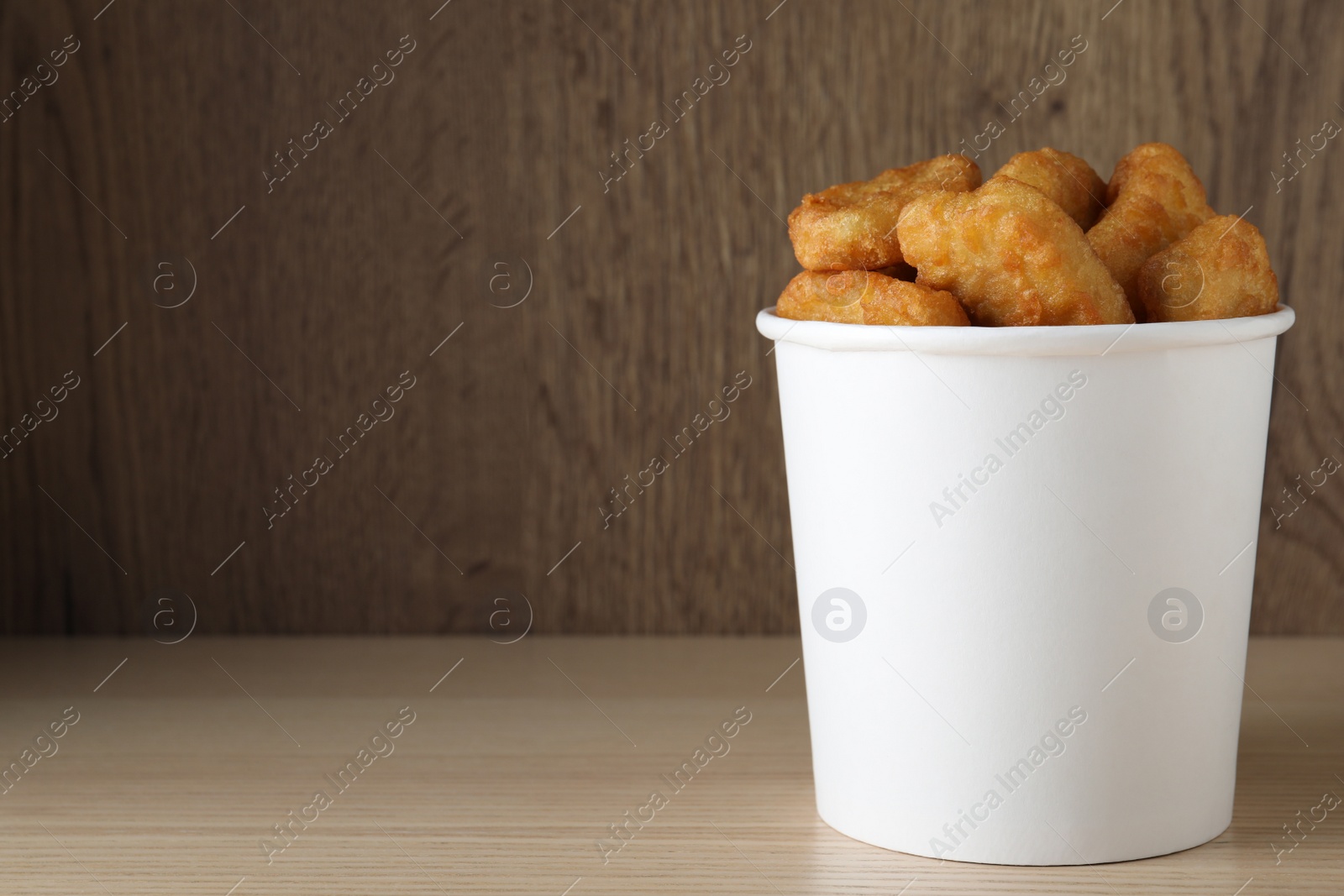 Photo of Bucket with tasty chicken nuggets on wooden table. Space for text