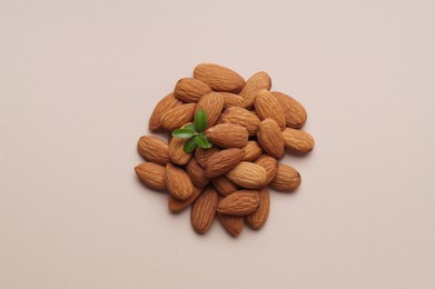 Delicious almonds and fresh leaves on beige background, top view