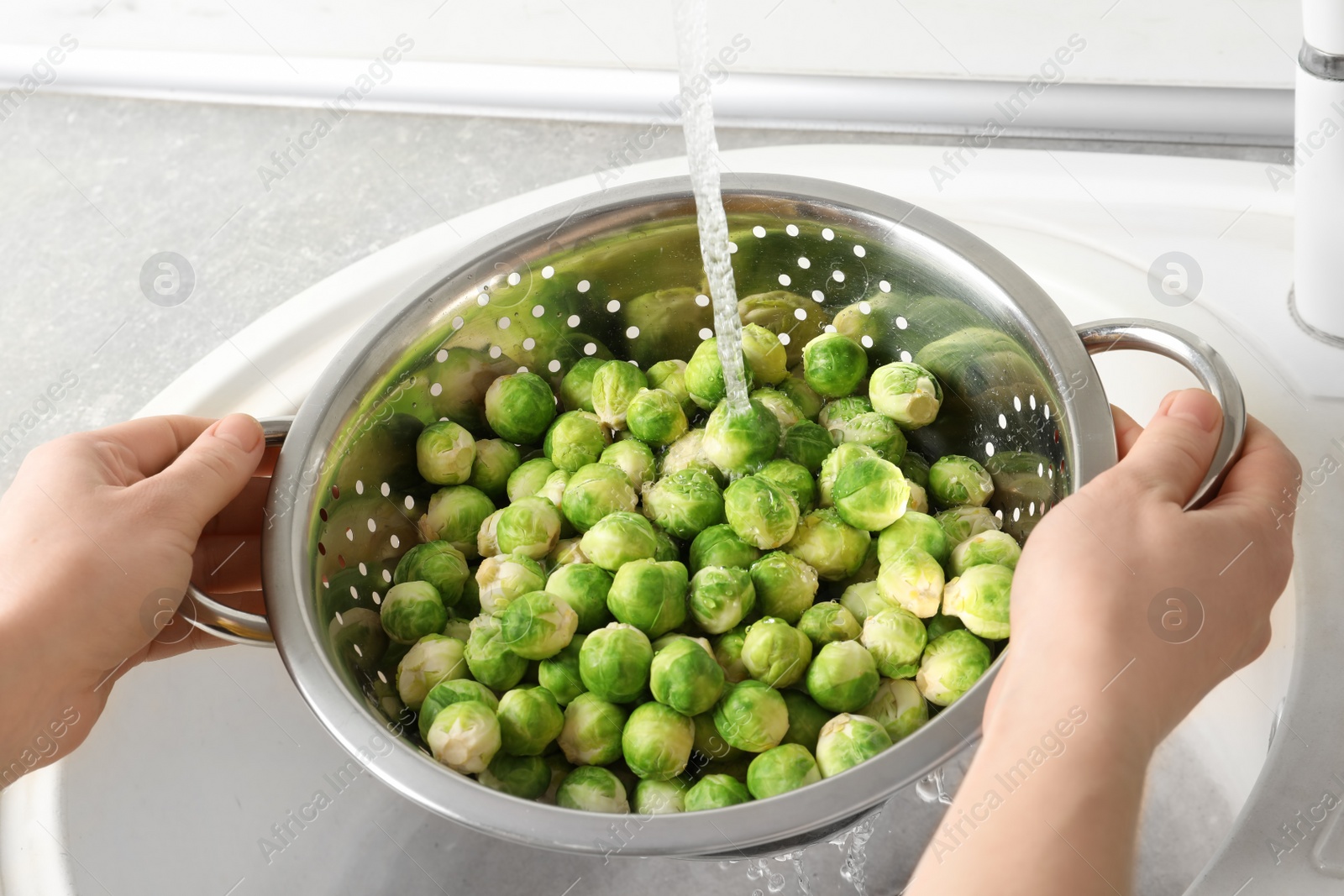 Photo of Woman washing fresh Brussels sprouts in colander, closeup