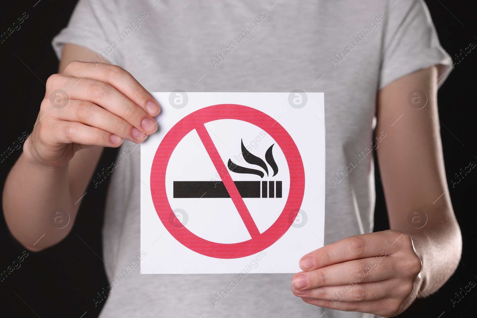 Photo of Woman holding card with no smoking sign on black background, closeup